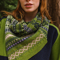 model standing in the woods with a patterned twisted knitted snood in creens, blues and creams.