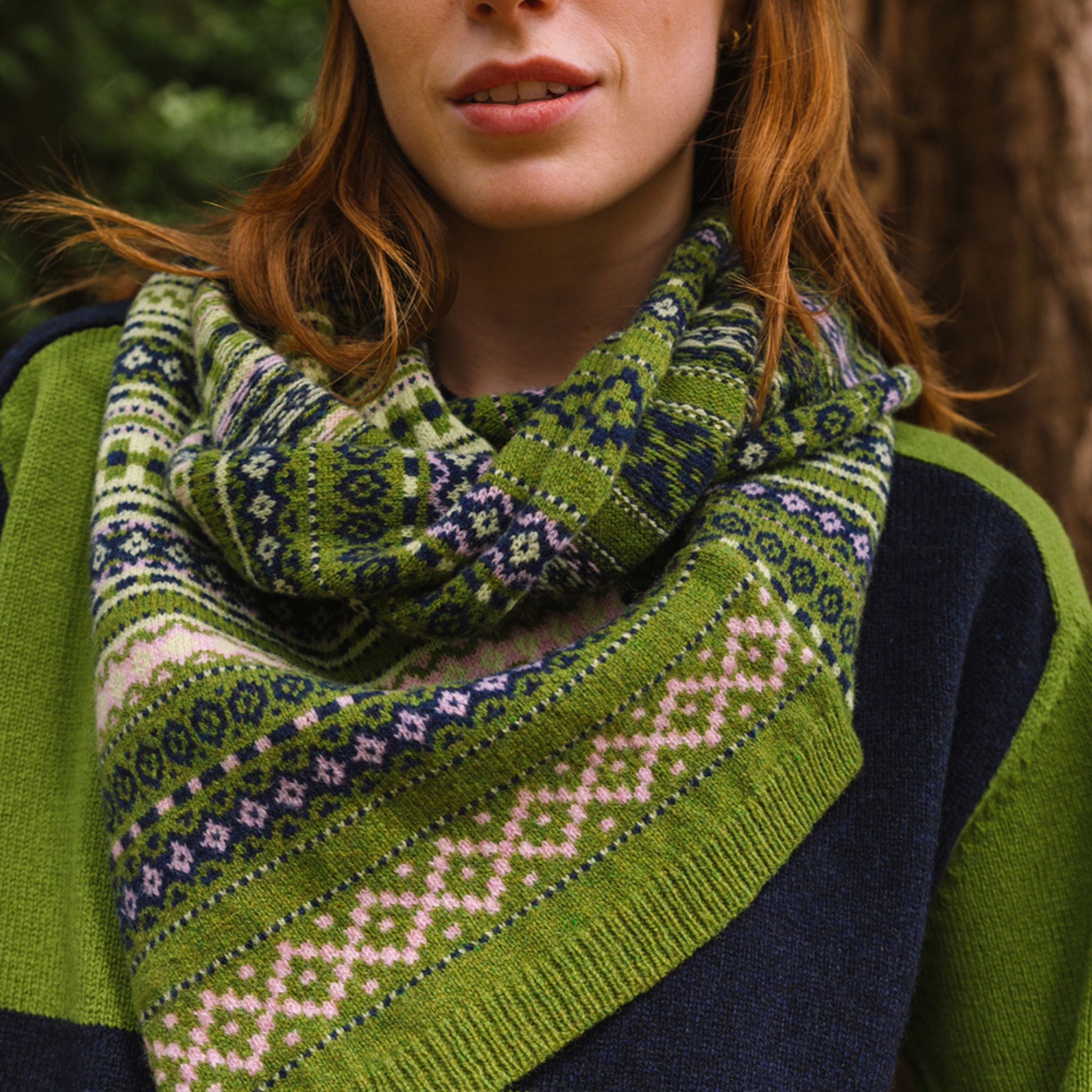 model standing in the woods with a patterned twisted knitted snood in creens, blues and creams.