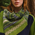 model standing in the woods with a patterned twisted knitted snood in creens, blues and creams.