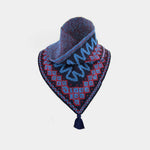 A knitted bandana-style neck warmer with a tassel, featuring a dark navy base with red and light blue geometric patterns and blue wavy accents, displayed on a light gray background.
