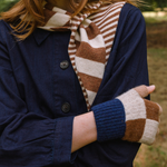 Person wearing a navy coat, striped scarf, and patterned gloves outdoors.
