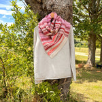 woollen with pink and red pattern draped over a light gray sweater against a natural background