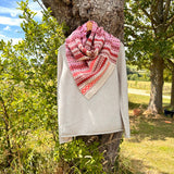 woollen with pink and red pattern draped over a light gray sweater against a natural background