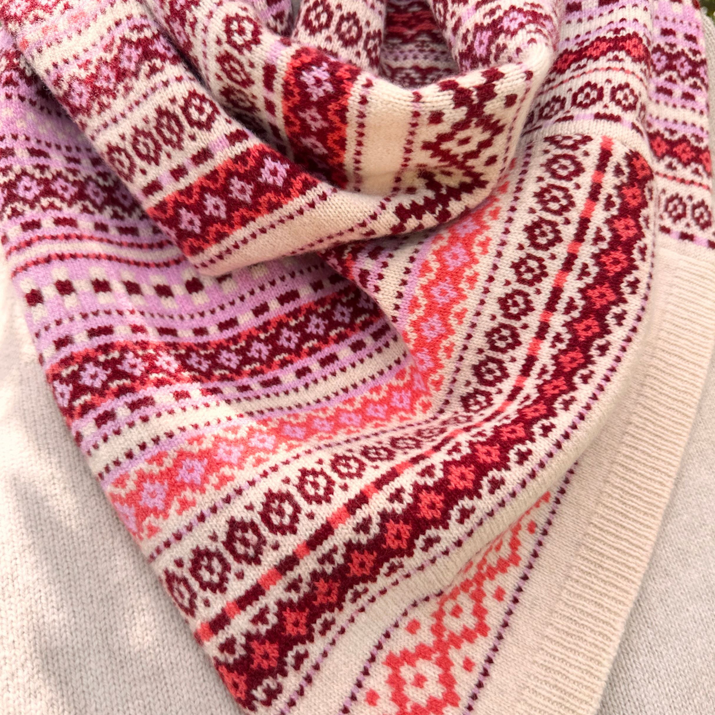 Close-up of a patterned scarf with red, pink, and white colors on a light gray background.