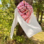 Pink patterned scarf draped over a gray top against a tree in a park setting.