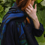 woman in a garden wearing a dark blue scarf with blue and green botanical patterns.