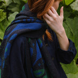 woman in a garden wearing a dark blue scarf with blue and green botanical patterns.