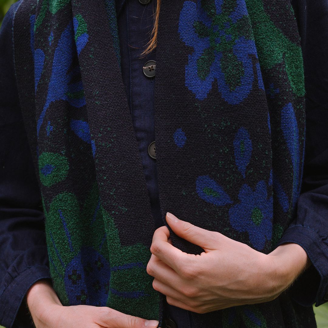 woman in a garden wearing a dark blue scarf with blue and green botanical patterns.