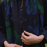 woman in a garden wearing a dark blue scarf with blue and green botanical patterns.