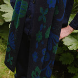 woman in a garden wearing a dark blue scarf with blue and green botanical patterns.