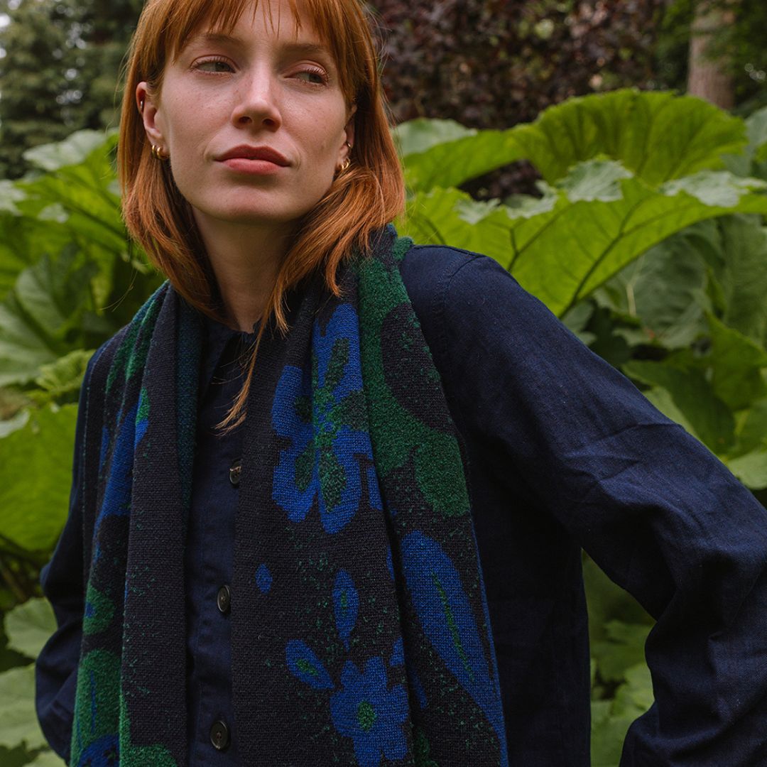 woman in a garden wearing a dark blue scarf with blue and green botanical patterns.