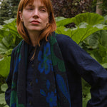 woman in a garden wearing a dark blue scarf with blue and green botanical patterns.