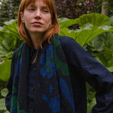 woman in a garden wearing a dark blue scarf with blue and green botanical patterns.