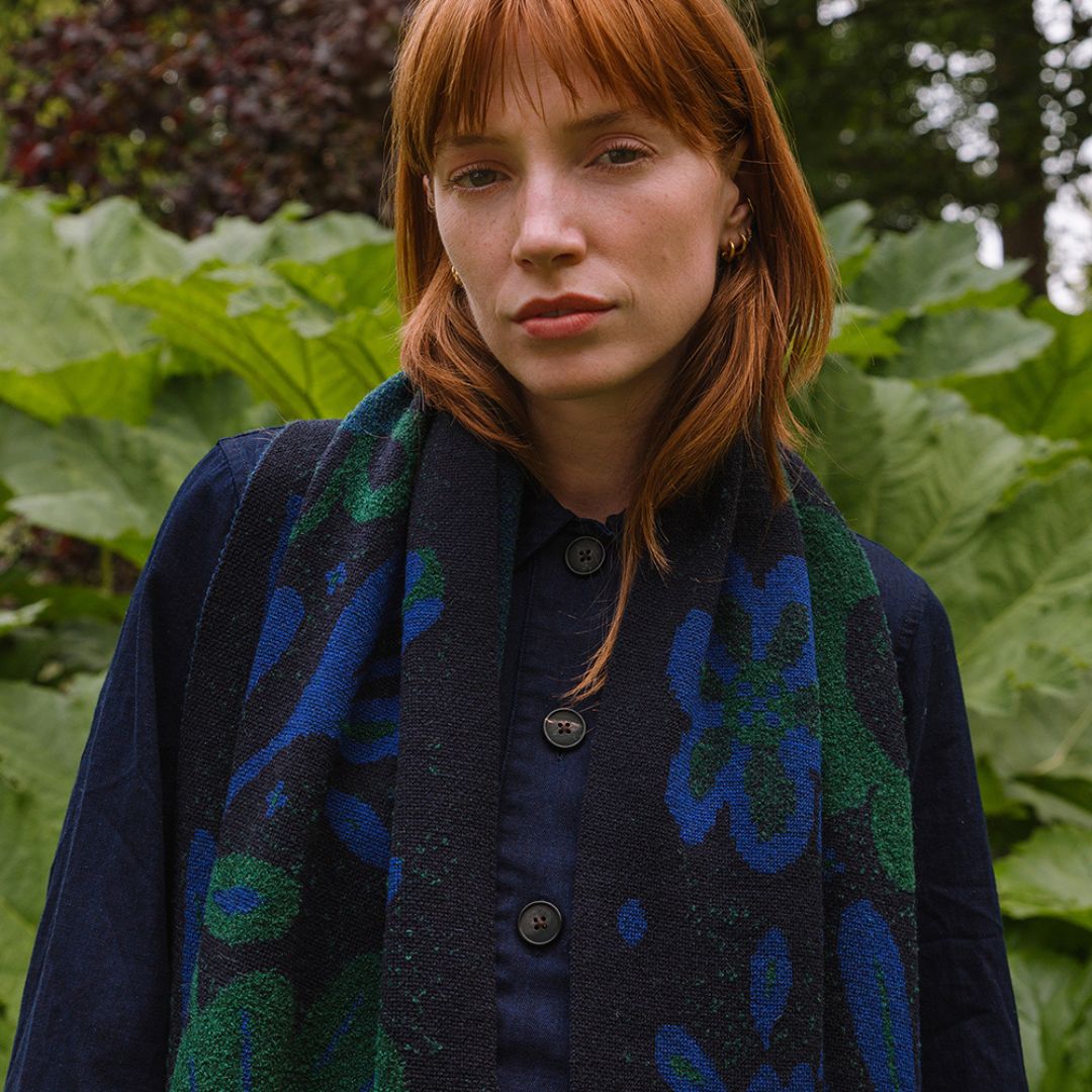 woman in a garden wearing a dark blue scarf with blue and green botanical patterns.