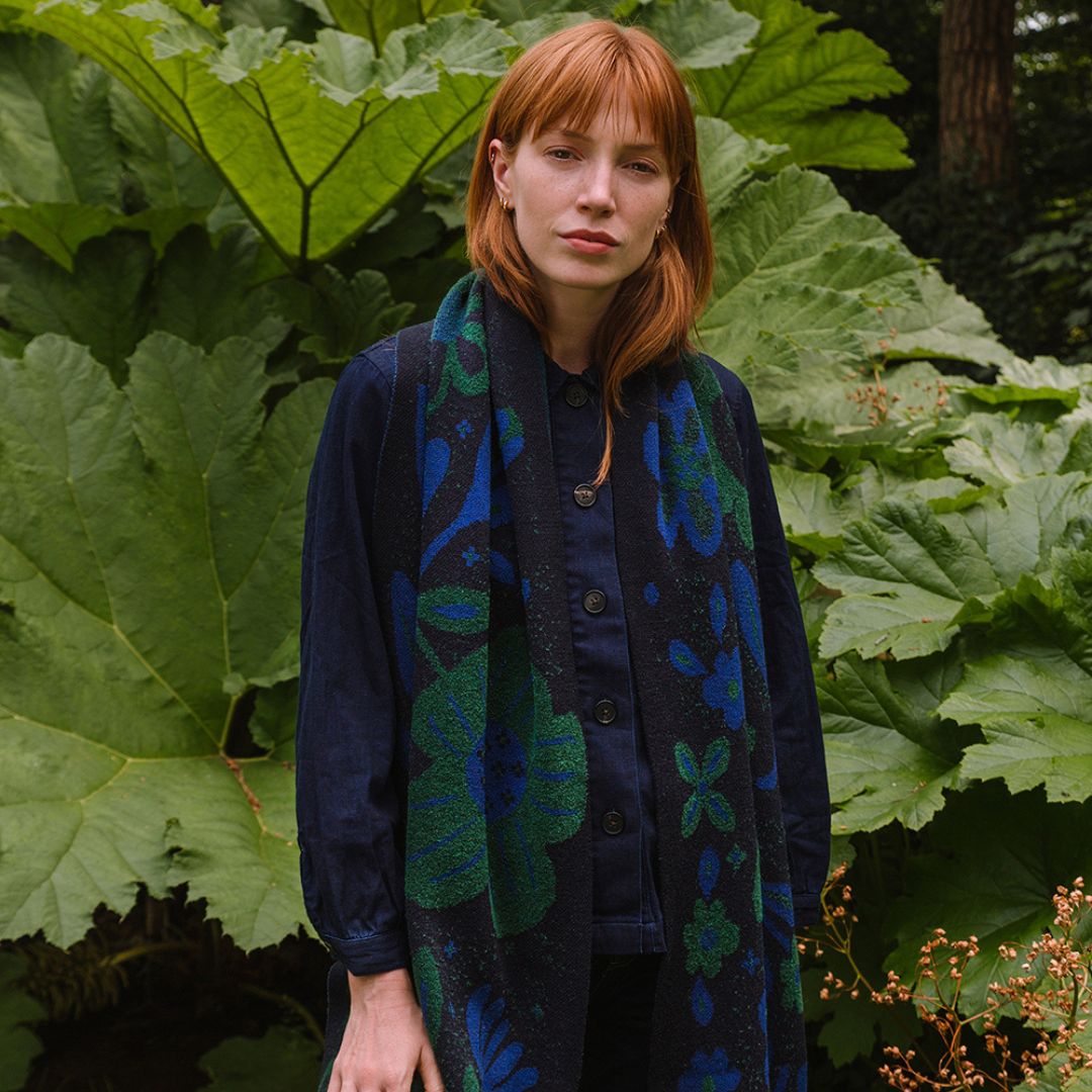woman in a garden wearing a dark blue scarf with blue and green botanical patterns.