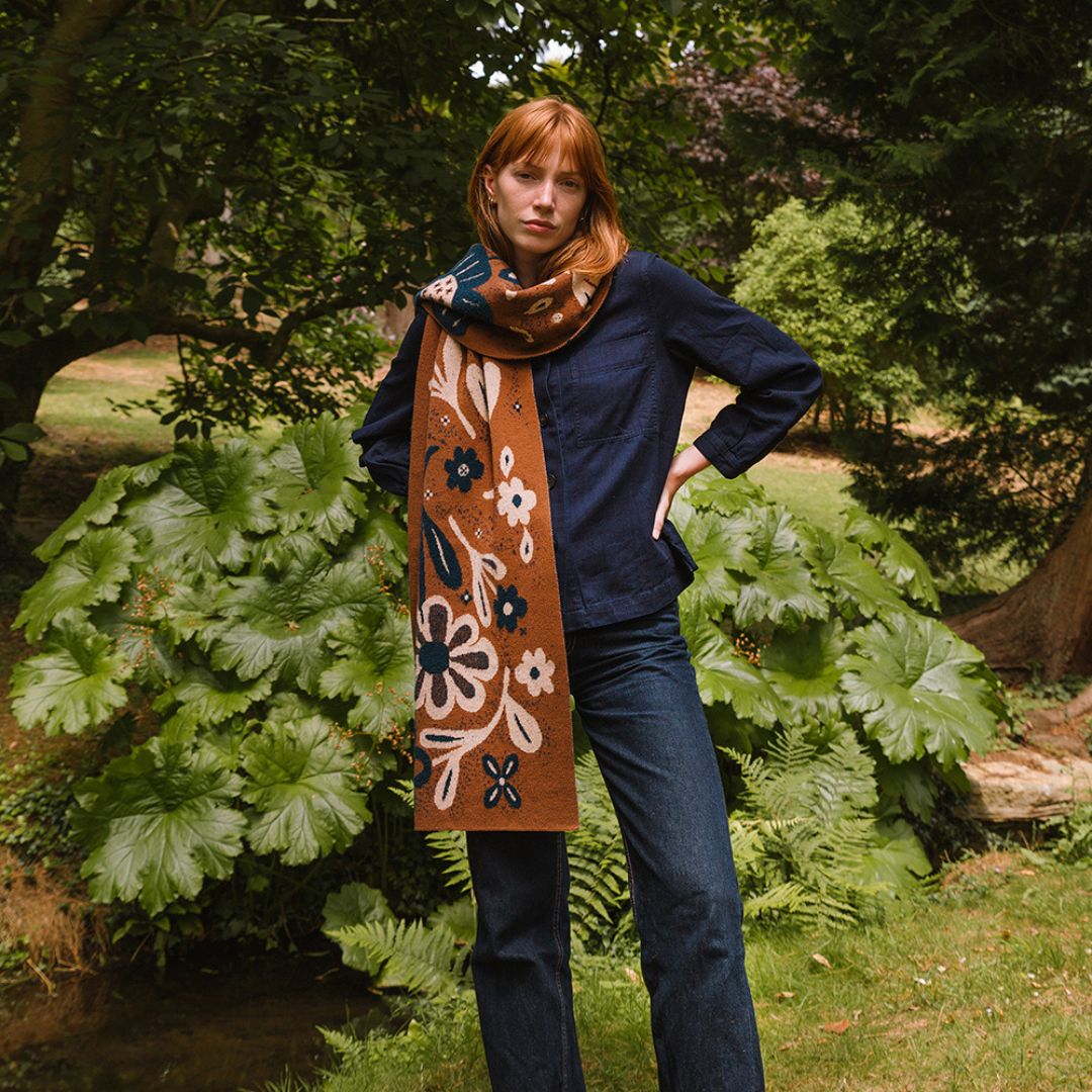 Person wearing a long, decorative scarf with floral patterns in a garden setting