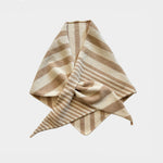A folded striped scarf or bandana made of soft woven fabric, featuring alternating beige and light brown horizontal stripes, presented on a clean light gray background.