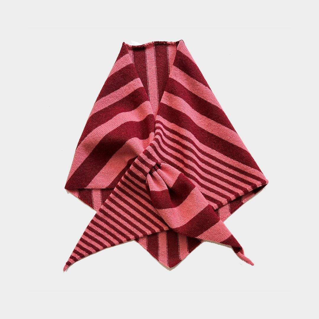 A folded striped knit scarf or bandana in shades of pink and deep red, arranged on a light gray background.