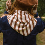 Person wearing a brown and white striped scarf, brown beanie, and gloves outdoors.
