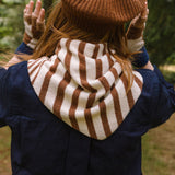 Person wearing a brown and white striped scarf, brown beanie, and gloves outdoors.