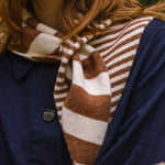 Close-up of a person wearing a brown and white striped scarf with a blue jacket.