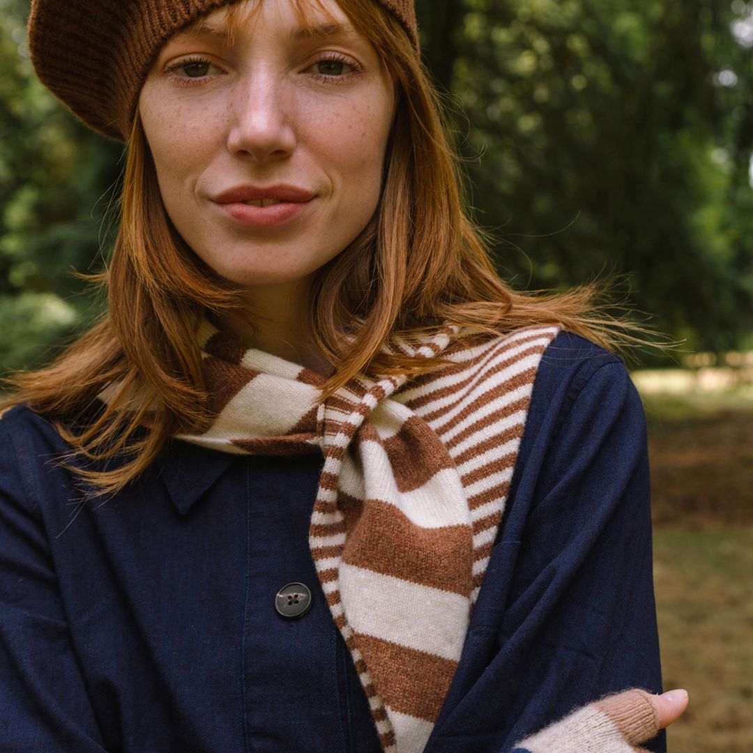 Woman wearing a brown beanie, striped scarf, and navy coat outdoors.