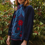 Person wearing a blue floral patterned scarf in front of green foliage