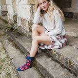 A woman sits on stone steps wearing a cream sweater, a red and white plaid skirt, and navy socks with a red and pink abstract pattern.