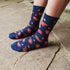A close-up of a person's feet wearing navy blue crew socks with a red, orange, and pink paisley pattern, standing on a stone pavement surface.
