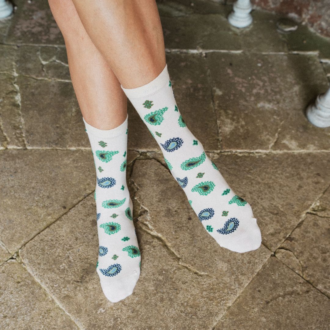 A person's legs wearing off-white crew socks with a green and blue paisley and clover pattern, standing on a stone tile floor.