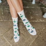 A person's legs wearing off-white crew socks with a green and blue paisley and clover pattern, standing on a stone tile floor.