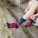 A person sitting on outdoor stone steps wearing navy blue crew socks with a red floral pattern.