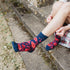 A person sitting on outdoor stone steps wearing navy blue crew socks with a red floral pattern.