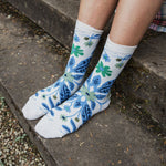 White crew socks with a blue and green floral pattern, worn by a person sitting on concrete outdoor steps.