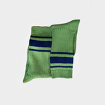 A pair of green knit crew socks with navy blue and white horizontal stripes near the cuff, displayed against a light gray background.