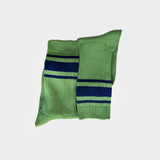 A pair of green knit crew socks with navy blue and white horizontal stripes near the cuff, displayed against a light gray background.