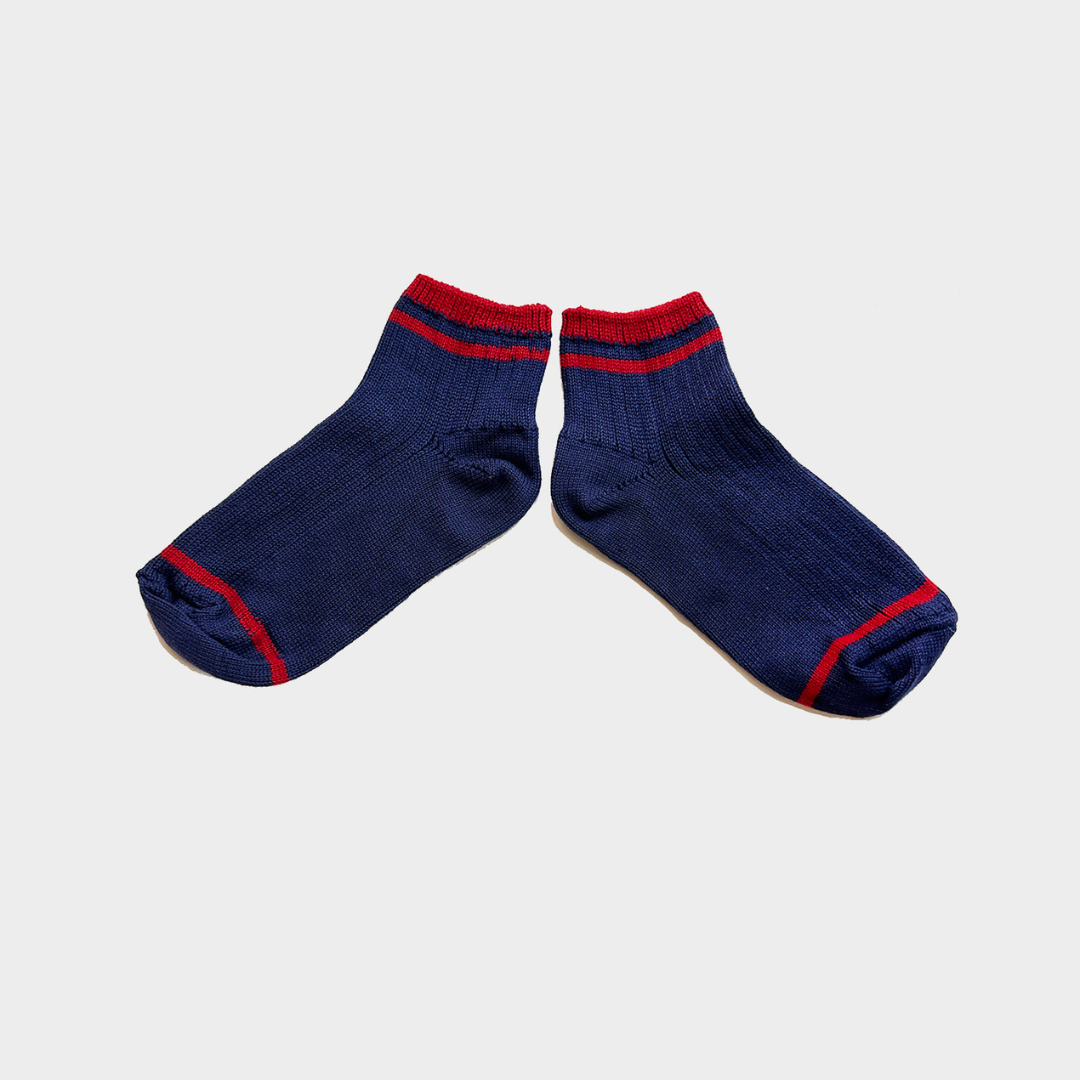 A pair of navy blue crew socks with red stripes at the ribbed cuffs and toes, displayed on a light gray background.