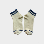 A pair of cream-colored ankle socks with navy blue stripes at the ribbed cuffs, heels, and toes, displayed against a light gray background.