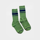A pair of green crew socks with navy blue horizontal stripes near the ribbed cuffs and navy blue trim on the toes, shown against a plain light gray background.
