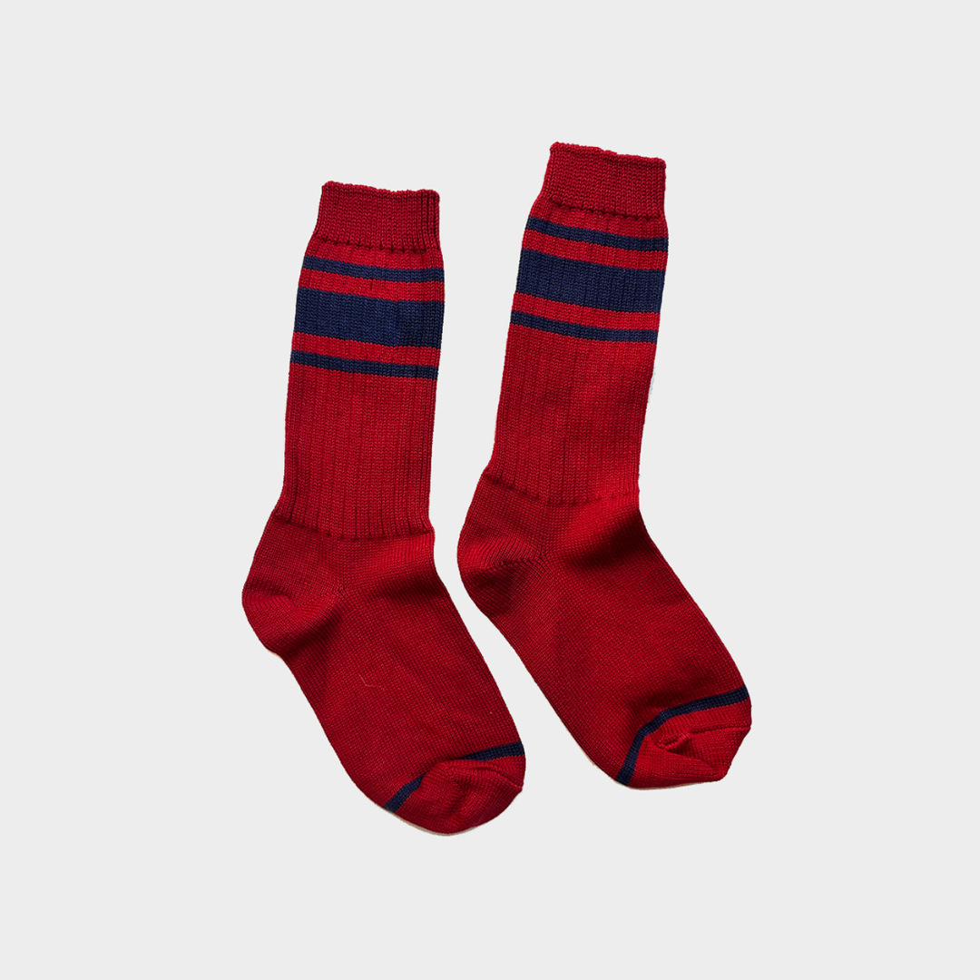 A pair of red crew socks with navy blue horizontal stripes near the cuff, displayed against a light gray background.