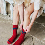 A person sitting on stone steps wearing red crew socks with navy and blue stripes, adjusting one sock with both hands.