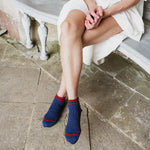 A person sitting on a stone bench wearing navy blue ankle socks with red stripes at the top, paired with a white dress.