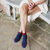 A person sitting on a stone bench wearing navy blue ankle socks with red stripes at the top, paired with a white dress.