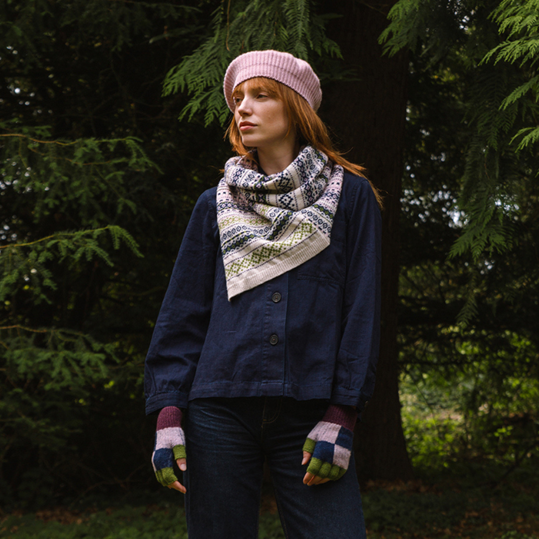 Person wearing a blue jacket, pink beret, and patterned scarf standing in a forest.