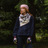 Person wearing a blue jacket, pink beret, and patterned scarf standing in a forest.
