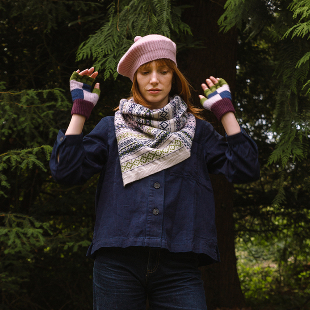 Person wearing a pink hat, patterned scarf, and colorful gloves standing in a forest.