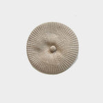 A round, ribbed knit cap in a light beige or oatmeal color, featuring a central button detail, photographed from directly above on a light gray background.