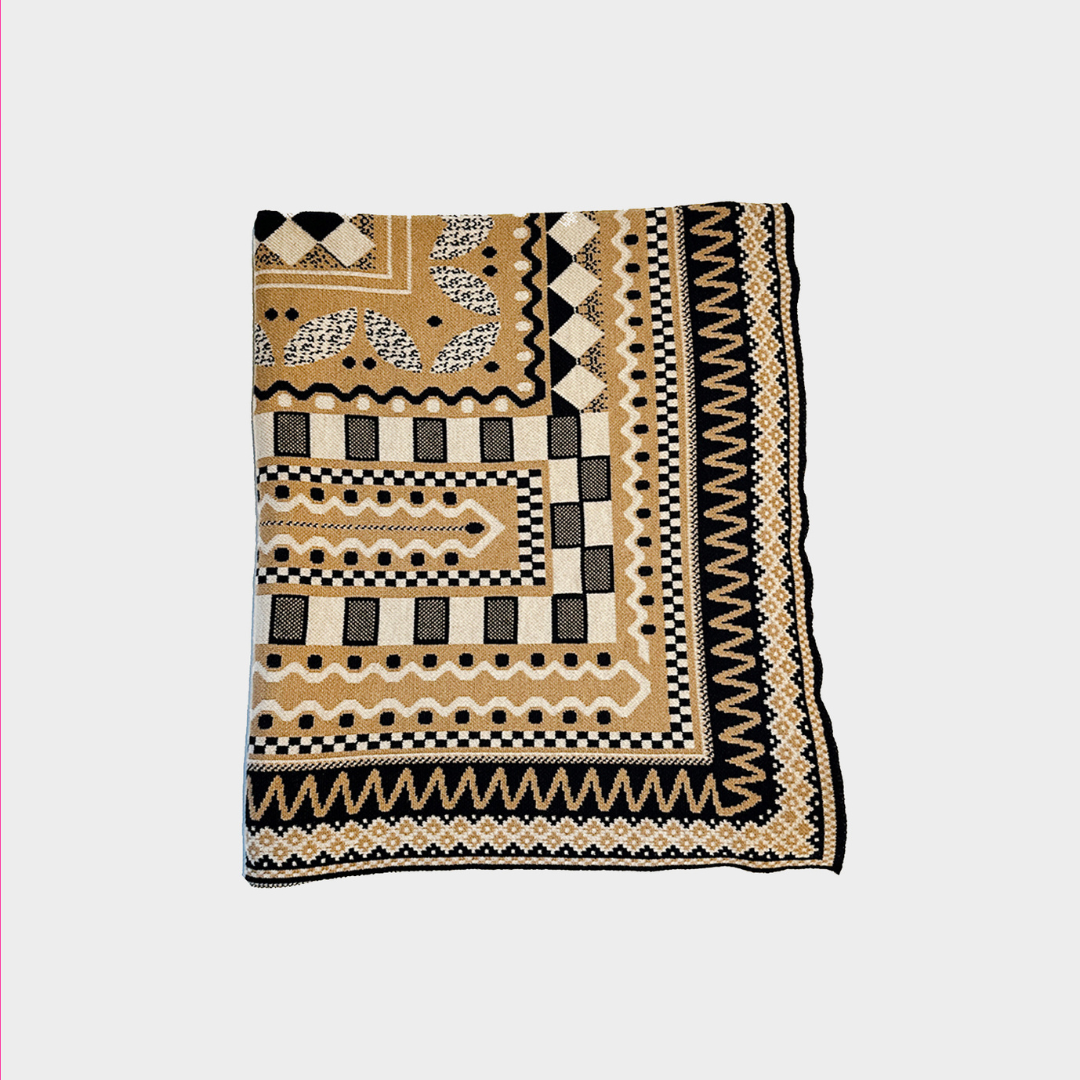 A folded patterned textile blanket or featuring a geometric tribal design in beige, black, and white on a light gray background.