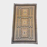 A knitted blanket with a geometric pattern in beige, and white, laid flat against a light gray background.