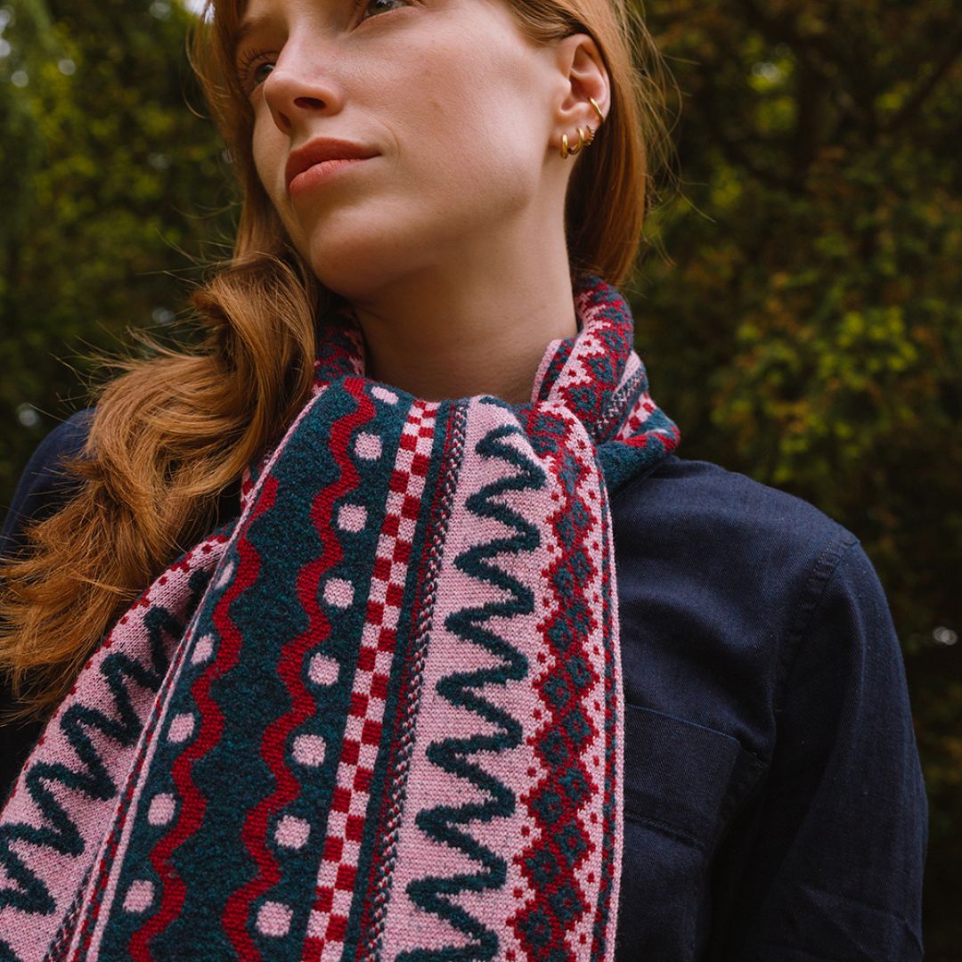 Person wearing a dark sweater and berry coloured patterned scarf standing in a forest setting
